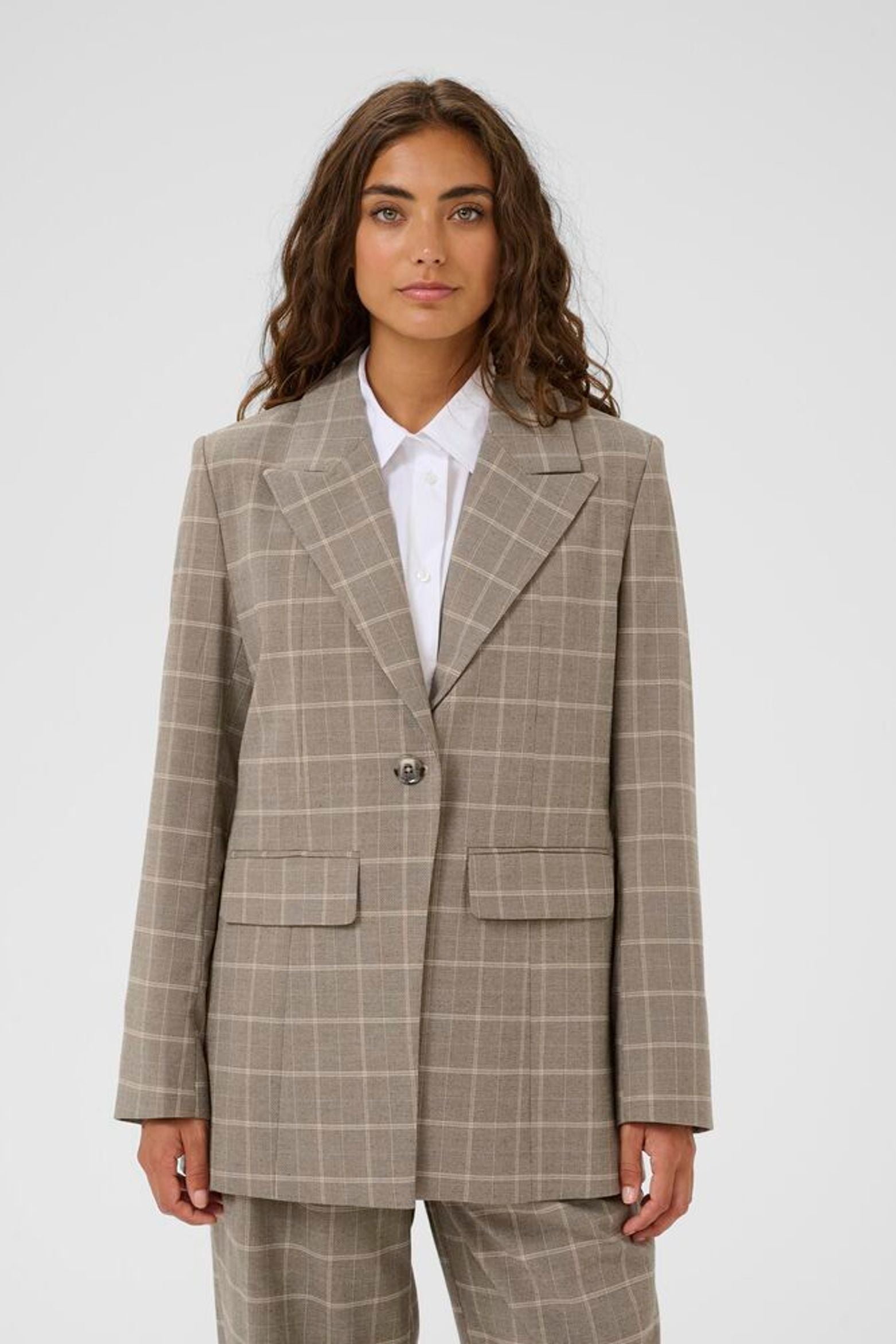 Woman wearing a brown checkered suit with a white shirt on a white background