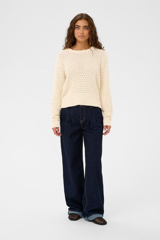 Woman wearing a cream textured sweater and navy pants on a white background