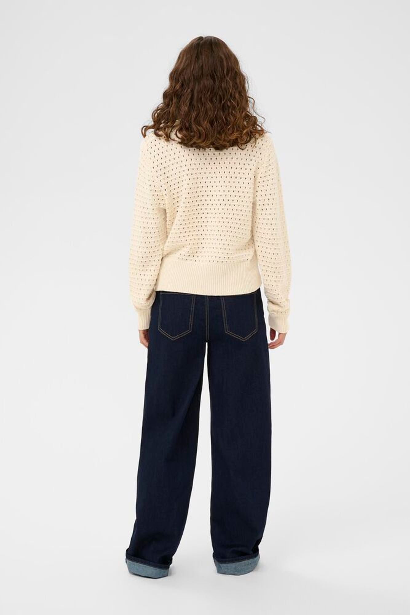Person wearing a beige patterned sweater and dark blue jeans on a white background