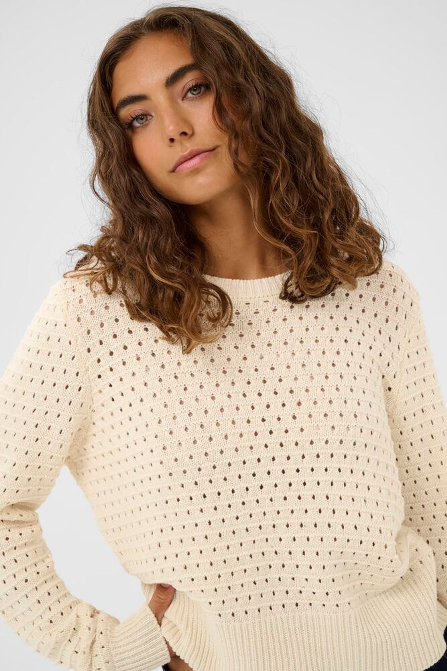 Woman wearing a beige knitted sweater against a plain background