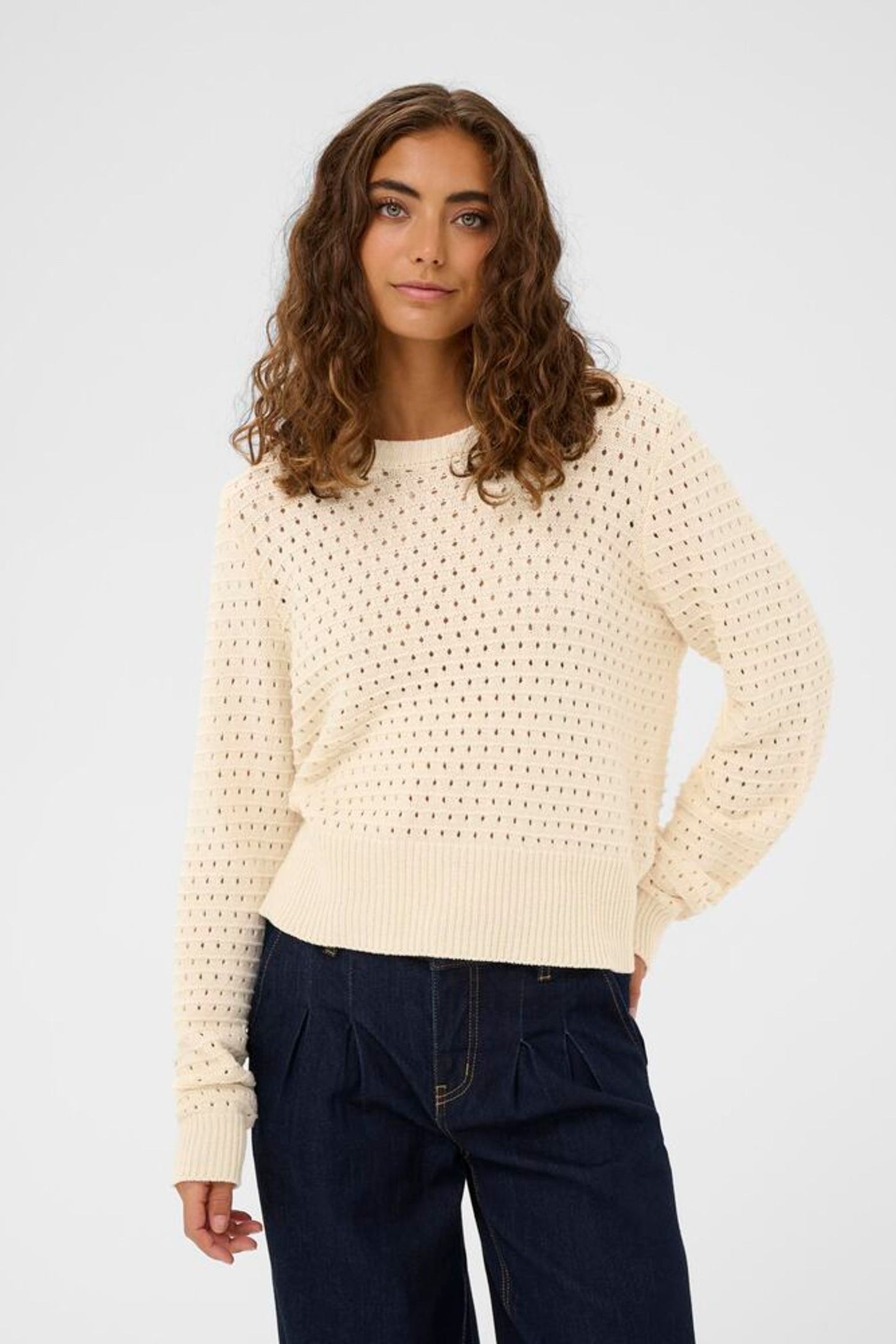 Woman wearing a cream knitted sweater and dark pants on a light gray background