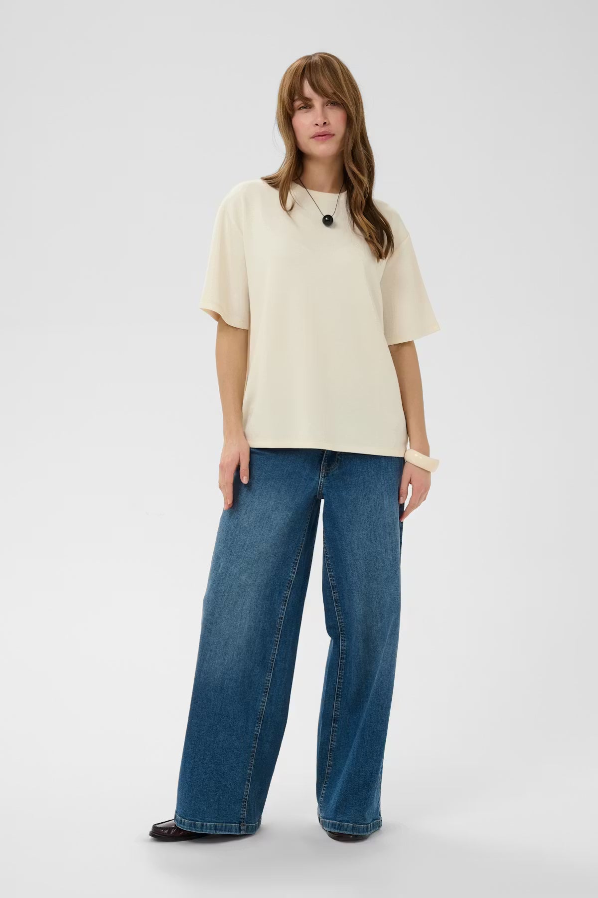 Woman wearing a beige top and blue jeans on a white background