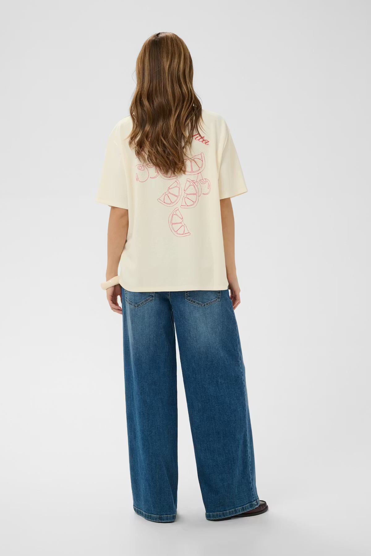 Person wearing a cream t-shirt with text and blue jeans on a white background