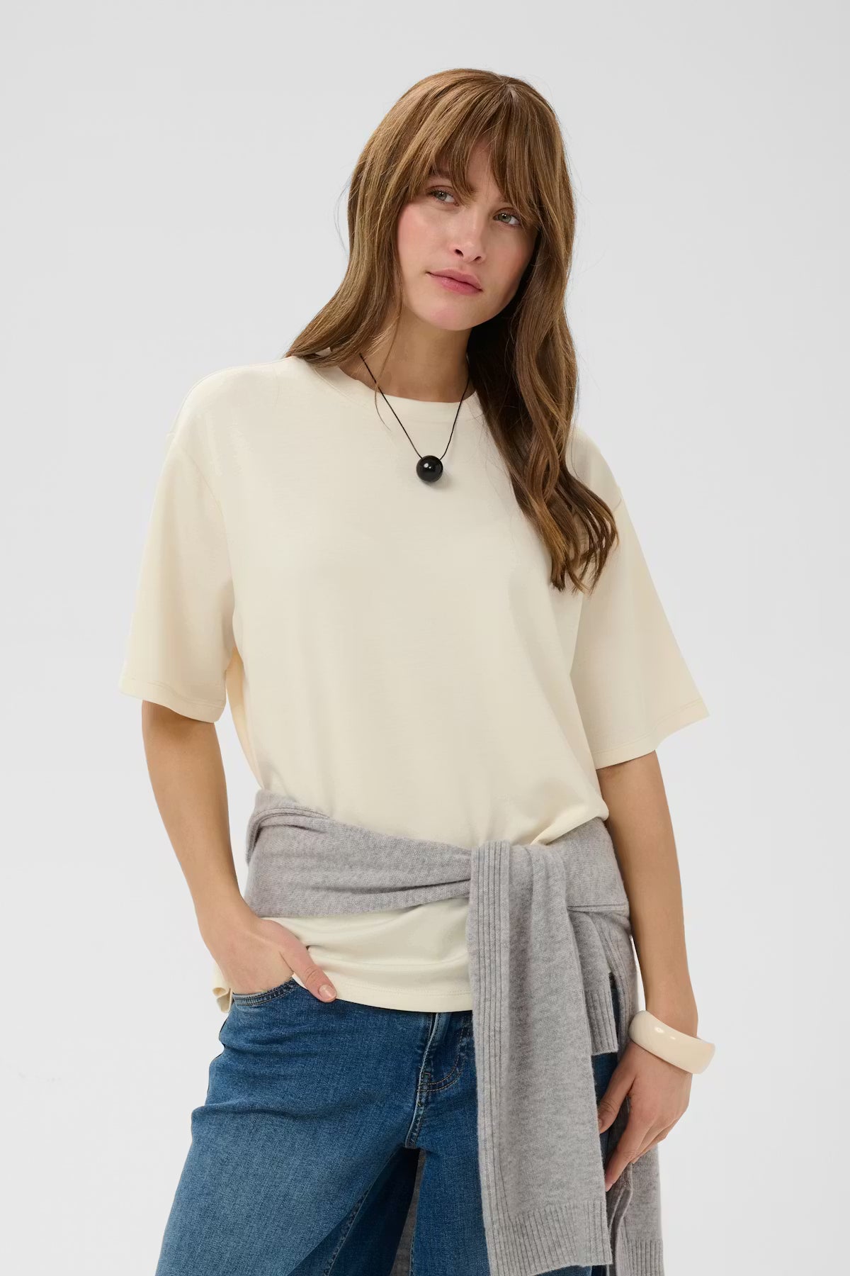 Woman wearing a cream top, blue jeans, and a gray scarf on a white background