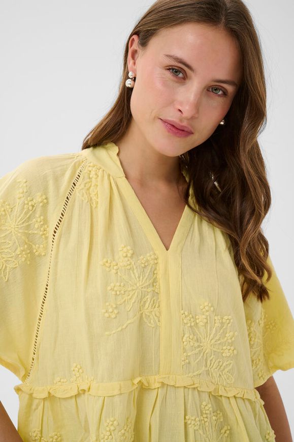 Woman wearing a yellow embroidered dress against a white background