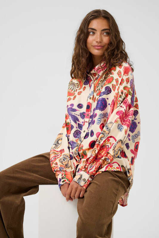 Woman wearing a colorful floral blouse and brown pants against a white background
