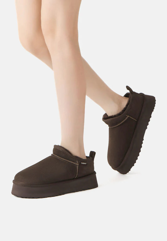 Brown winter boots worn with beige tights on a white background