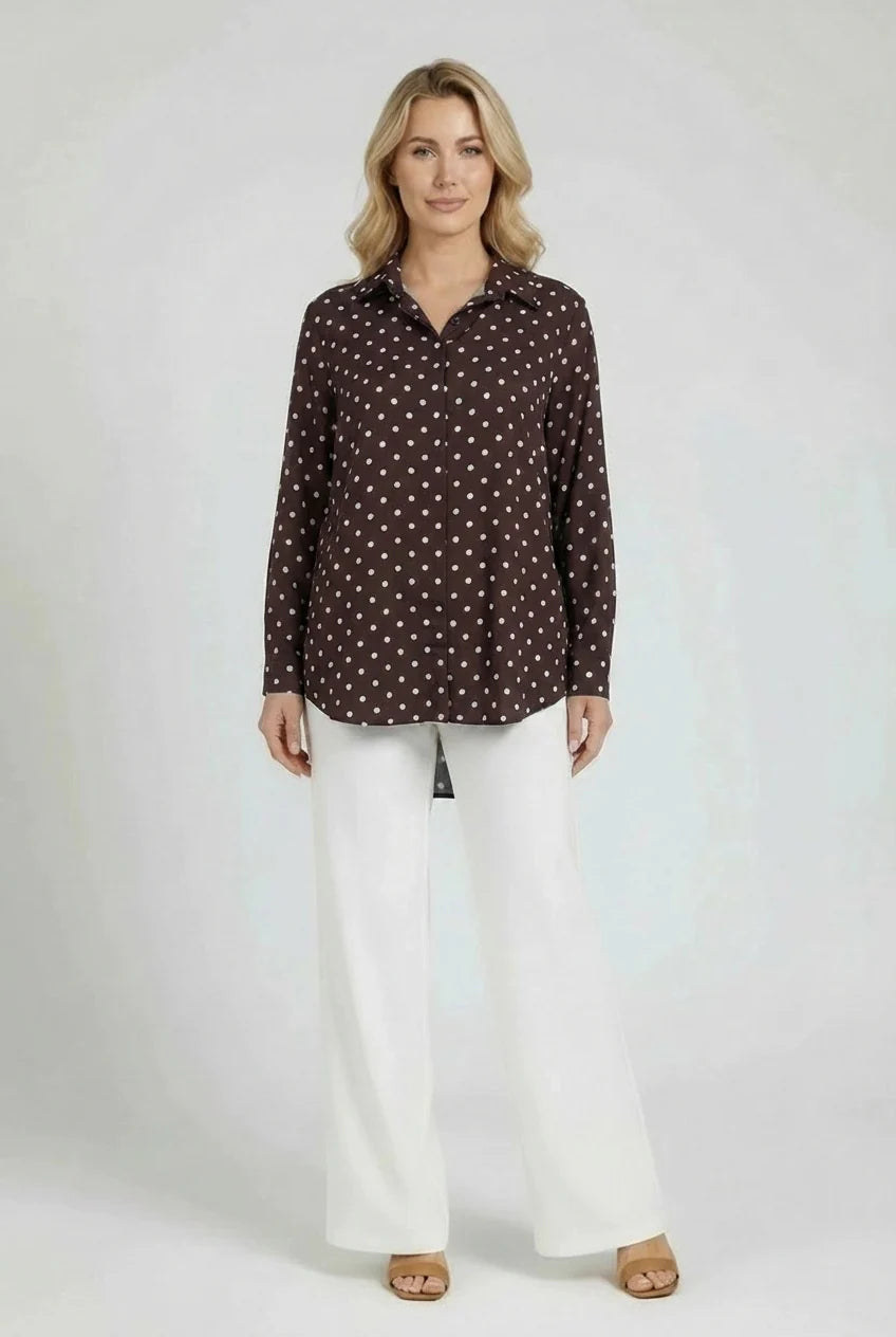 Woman wearing a brown polka dot blouse and white pants on a plain background