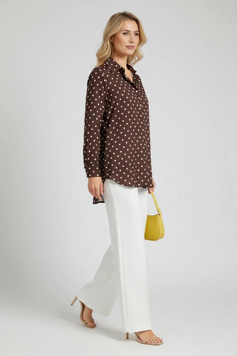 Woman wearing a brown polka dot shirt and white pants, holding a yellow bag on a white background
