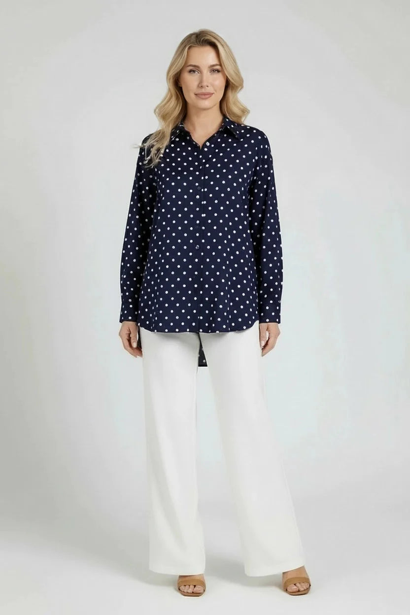 Woman wearing a navy polka dot shirt and white pants on a white background