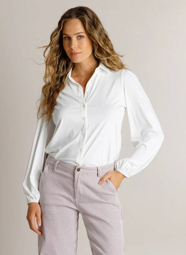 A woman modeling a white long-sleeve button-up shirt tucked into light pink and white vertically striped trousers, set against a plain light beige studio background.