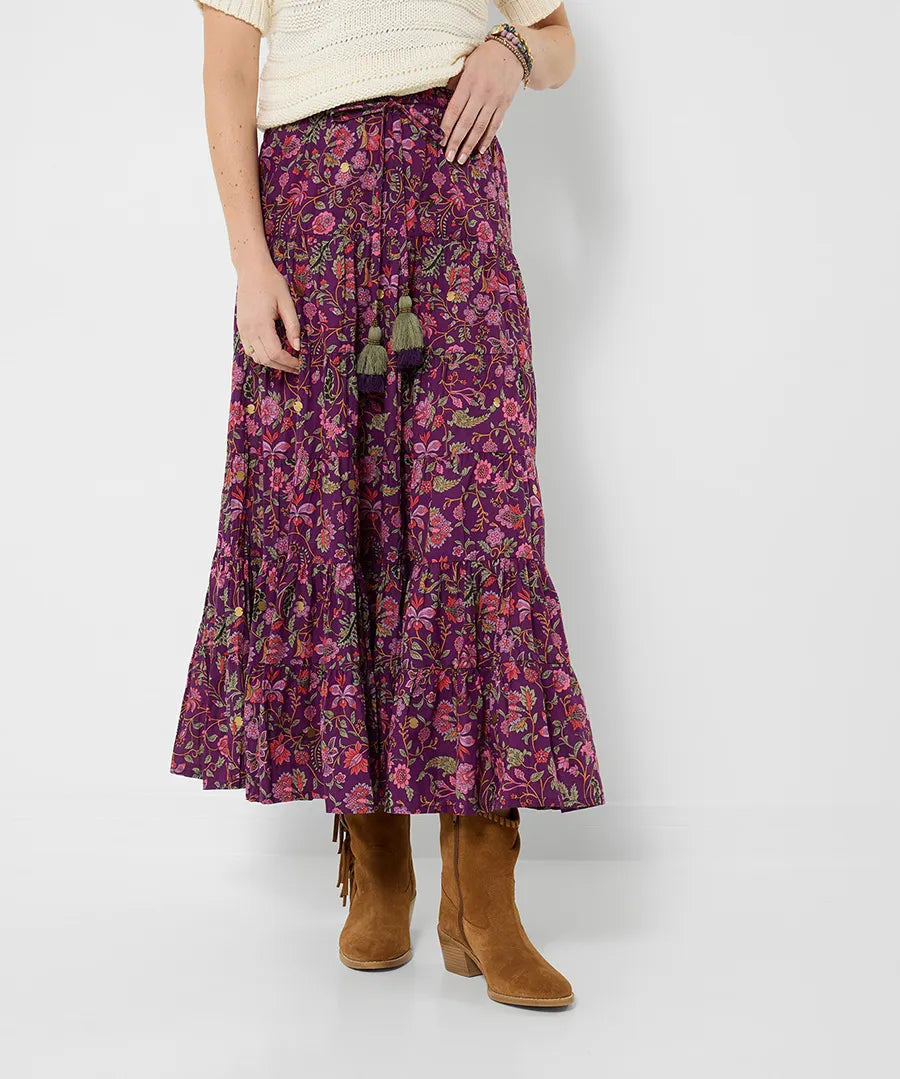 Person wearing a long floral skirt with tassels on a white background