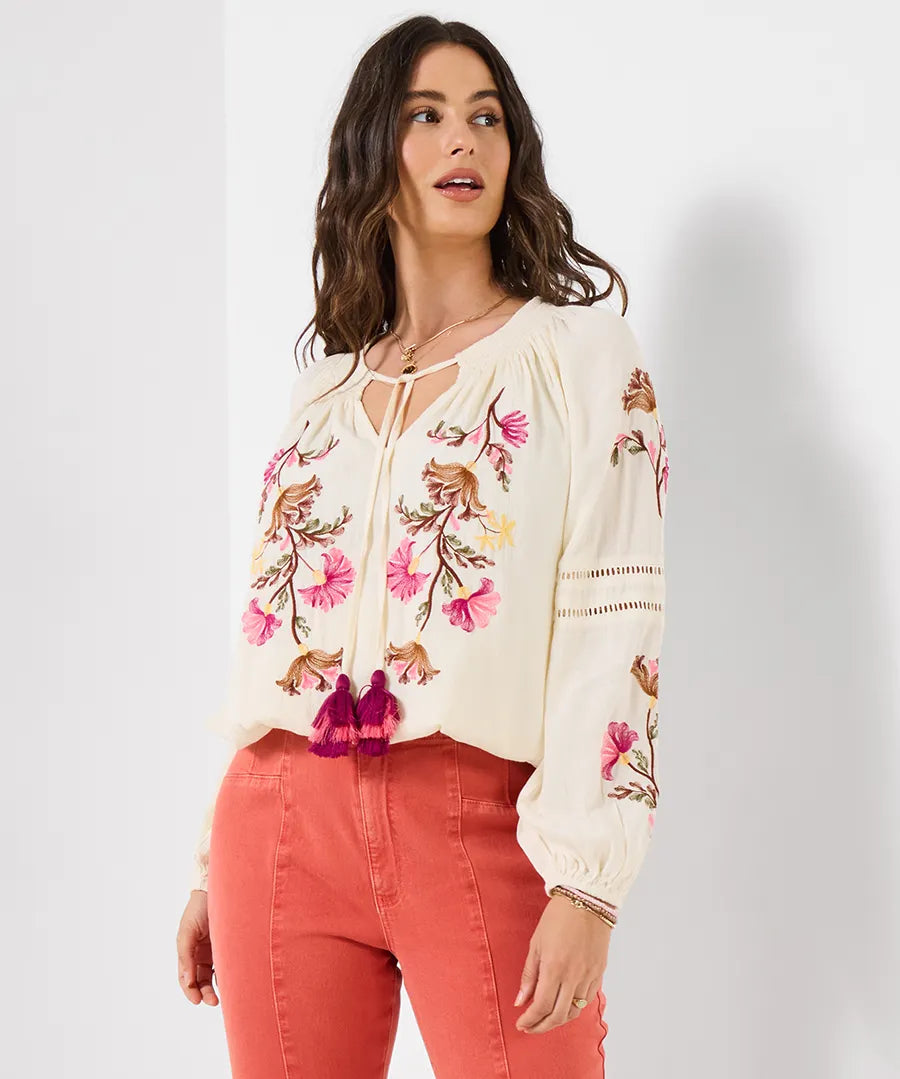 Woman wearing a white blouse with floral embroidery and red pants on a white background