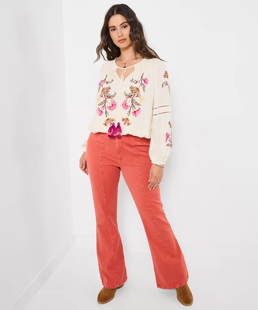 Woman wearing a floral embroidered top and red pants on a white background