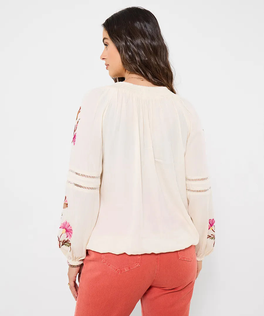Woman wearing a cream blouse with floral embroidery and pink pants on a white background