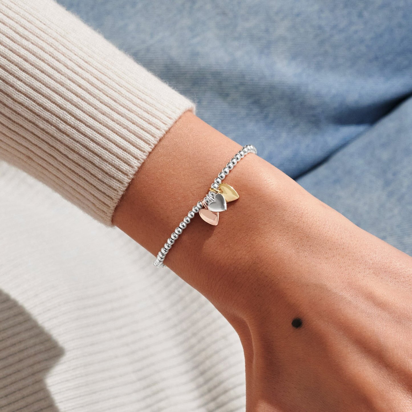 Close-up of a wrist wearing a silver bracelet with heart charms against a neutral background