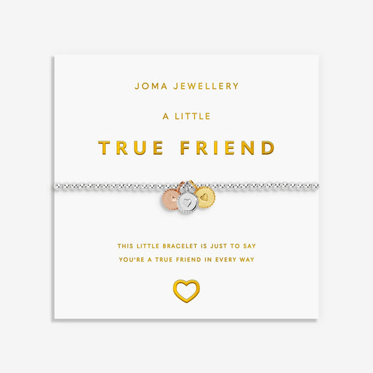 A silver friendship bracelet with three small charms (rose gold, silver, and gold) displayed on its white Joma Jewellery gift card, which features gold lettering and a gold heart outline.
