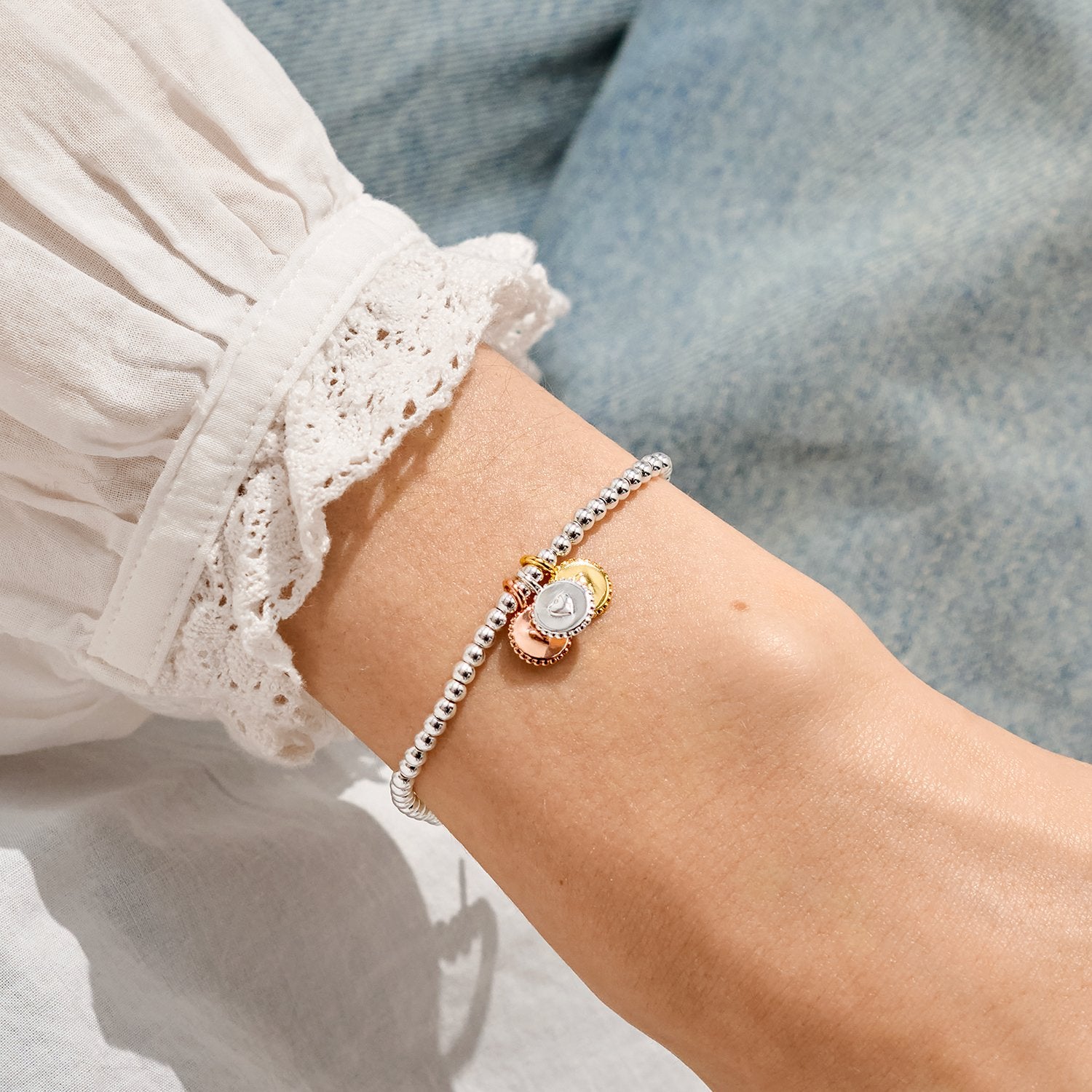 Close-up of a wrist wearing a silver and gold bracelet with a clear gemstone, against a blurred background.
