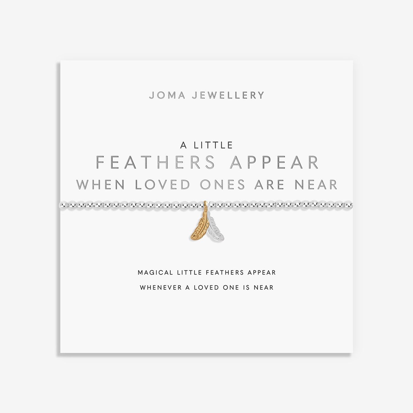 A delicate bracelet displayed on a white Joma Jewellery card. The bracelet features a silver-toned beaded line with a small gold-toned feather charm and a tiny white feather charm.