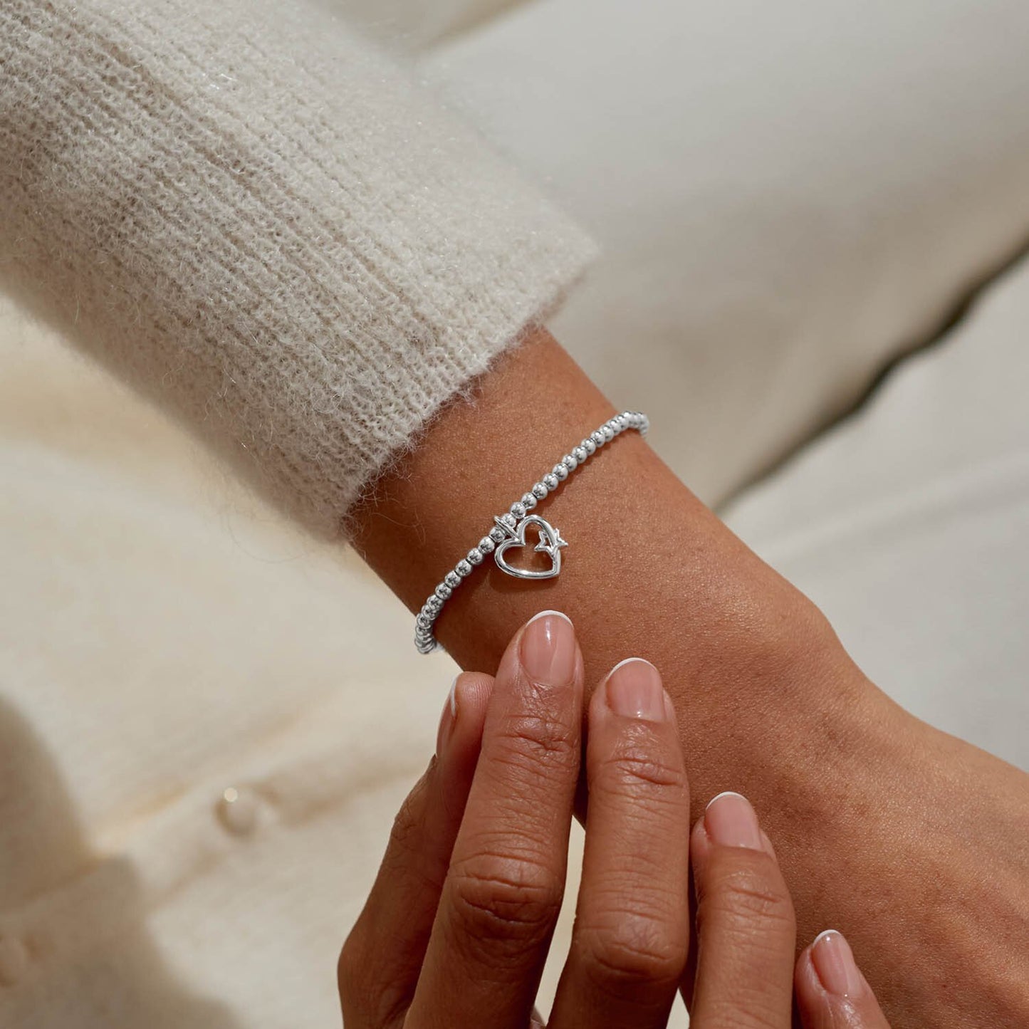Silver bracelet with a heart charm on a wrist against a neutral background