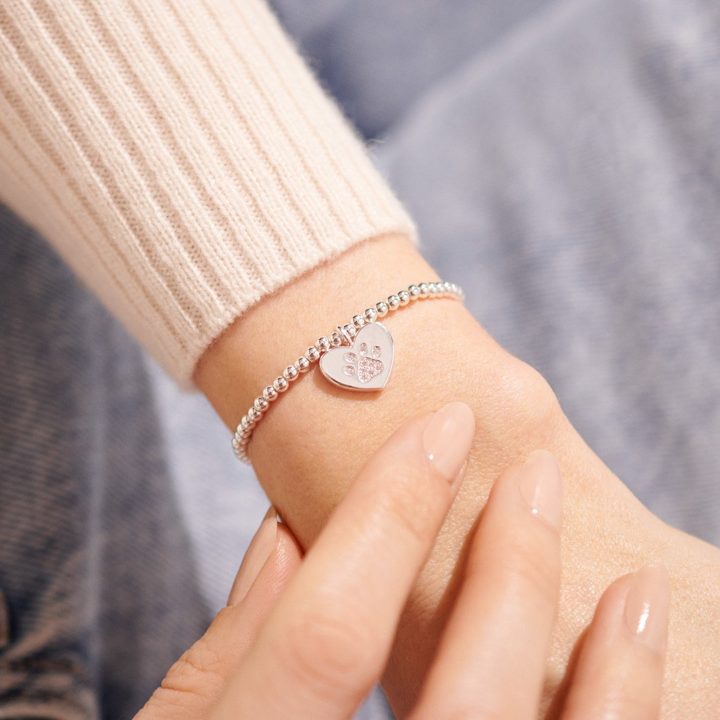 Close-up of a person wearing a silver bracelet with a heart-shaped charm on a blurred background