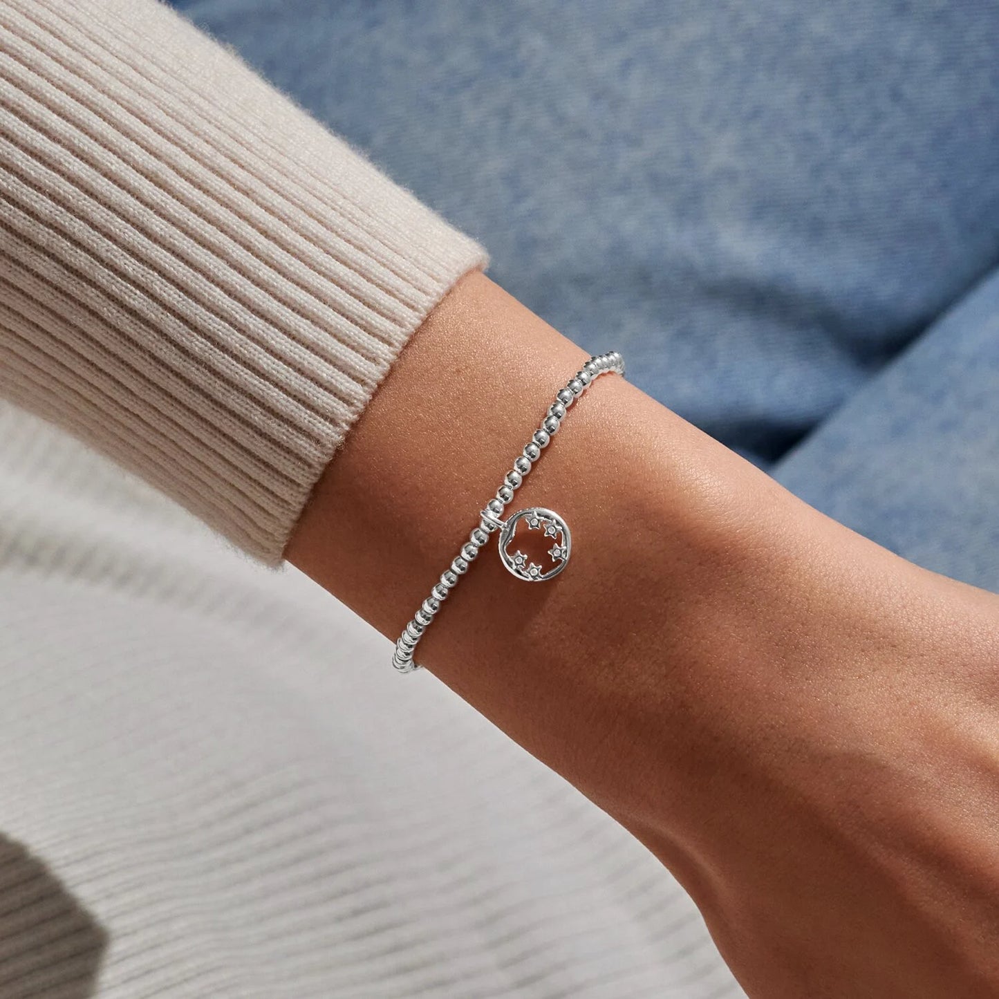 Silver bracelet with a round gemstone on a wrist against a neutral background