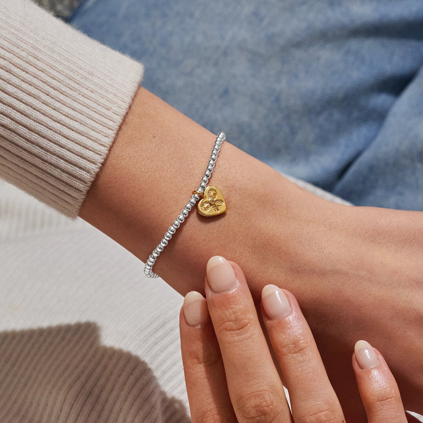 Close-up of a wrist wearing a gold heart-shaped bracelet with a blurred background