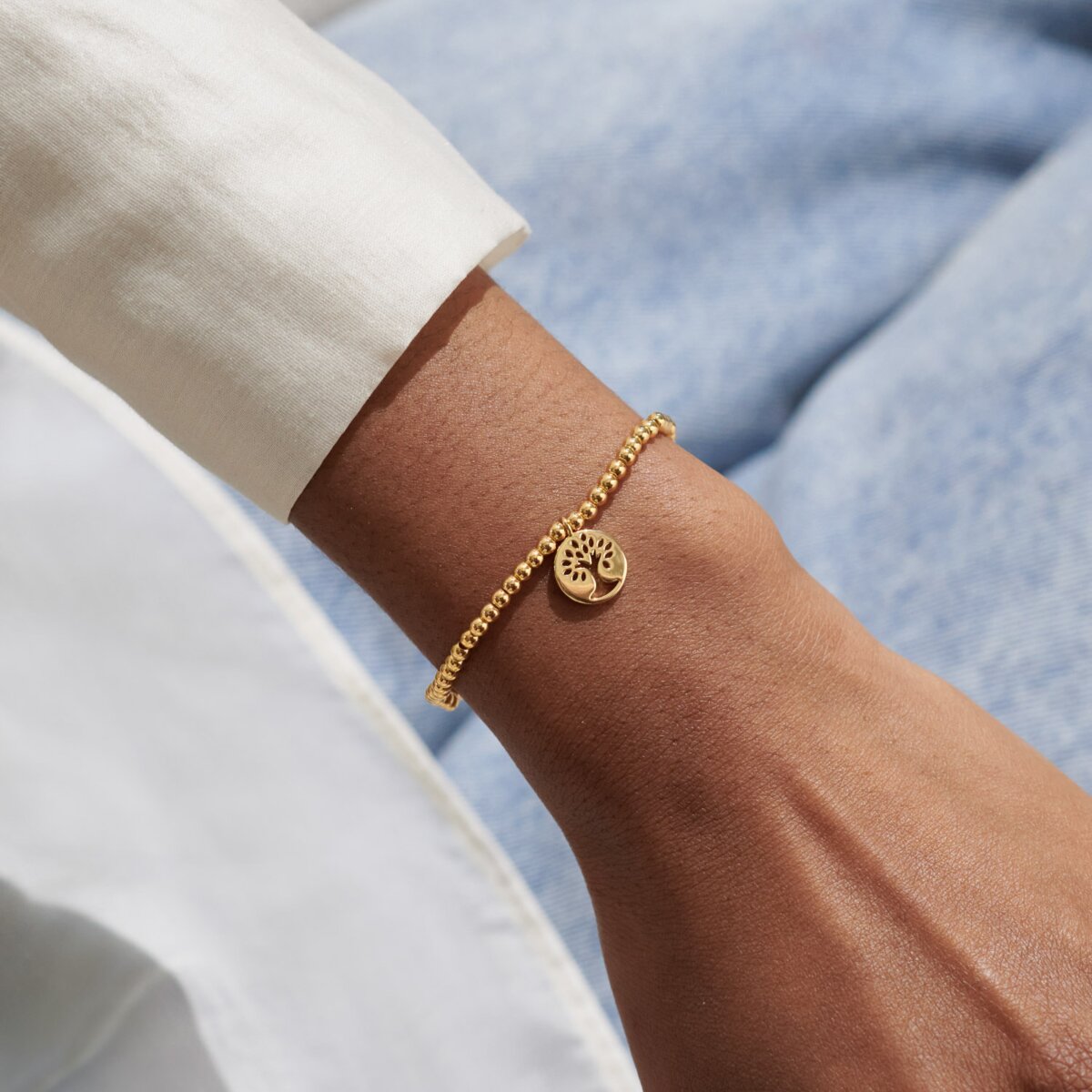Gold bracelet with a tree of life charm on a wrist against a light blue background