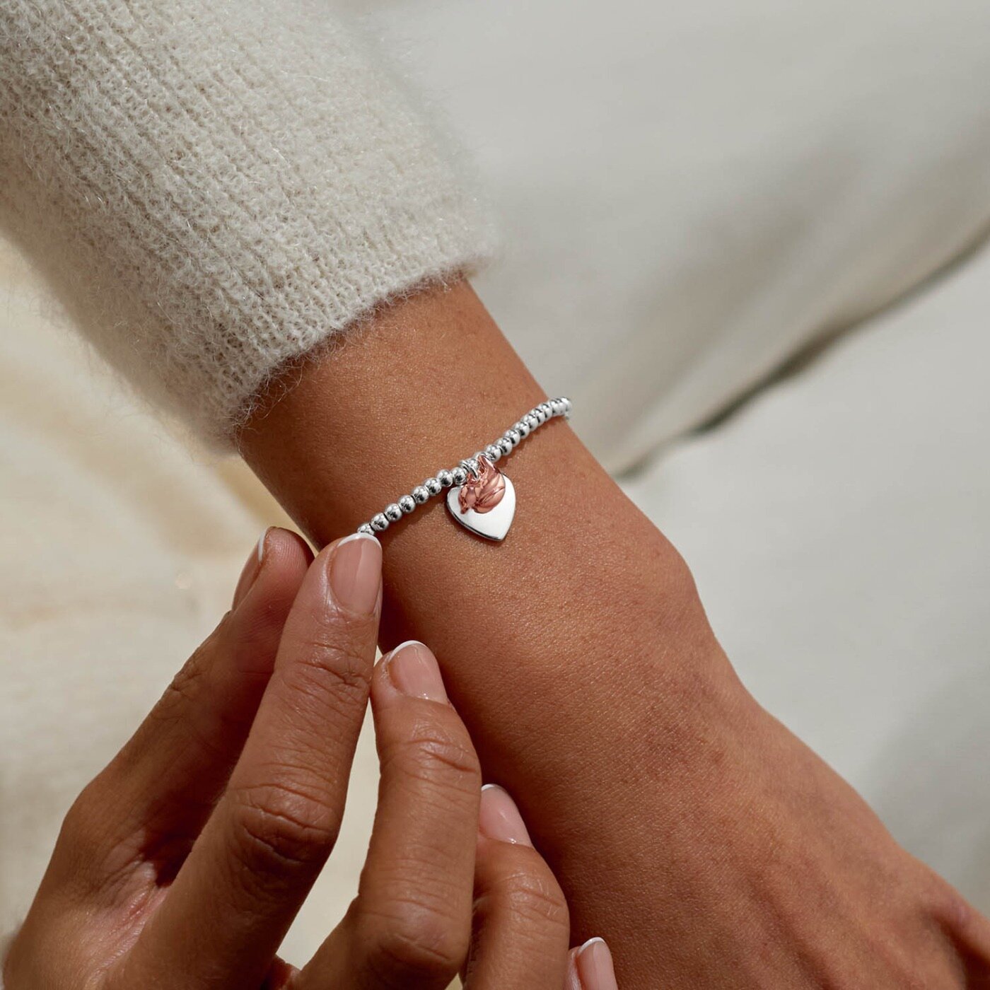 Silver bracelet with a heart charm on a wrist against a neutral background