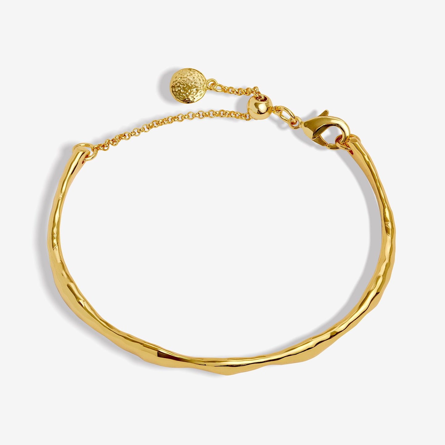A gold-toned bangle bracelet with a textured, hammered finish, a delicate chain extender, and a small round textured charm, shown on a light gray background.