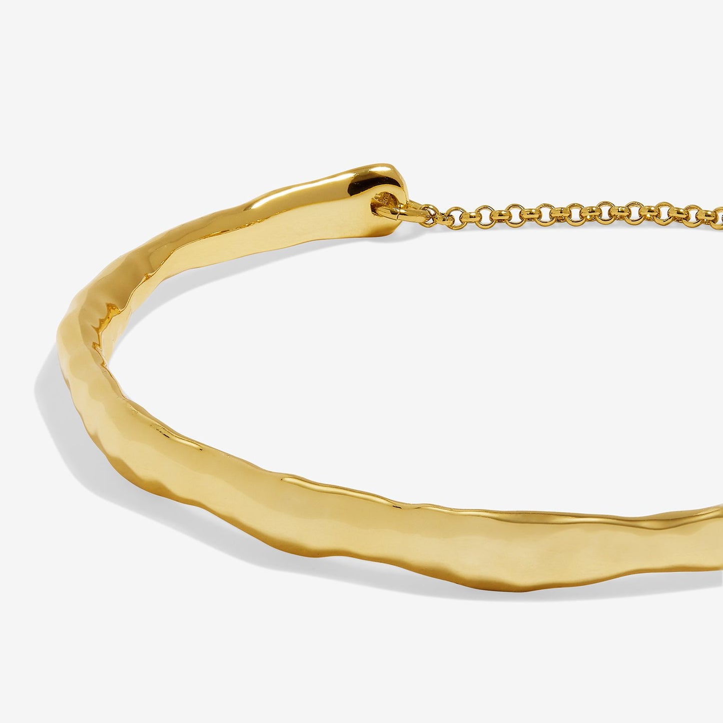 A close-up of a gold bangle bracelet with a hammered, organic textured finish and a matching gold chain extender, shown on a light gray background.