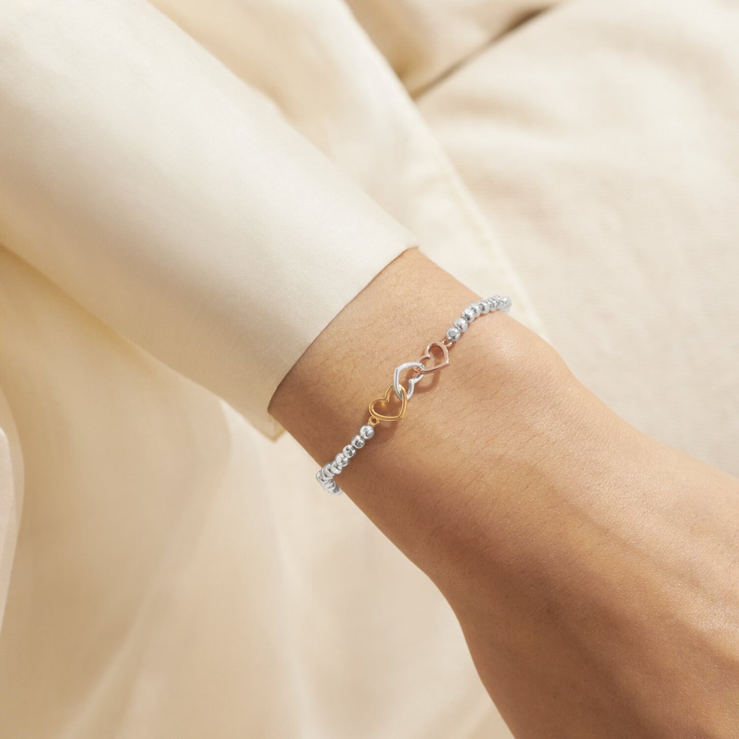 Bracelet with interlocking heart charms on a wrist against a beige background