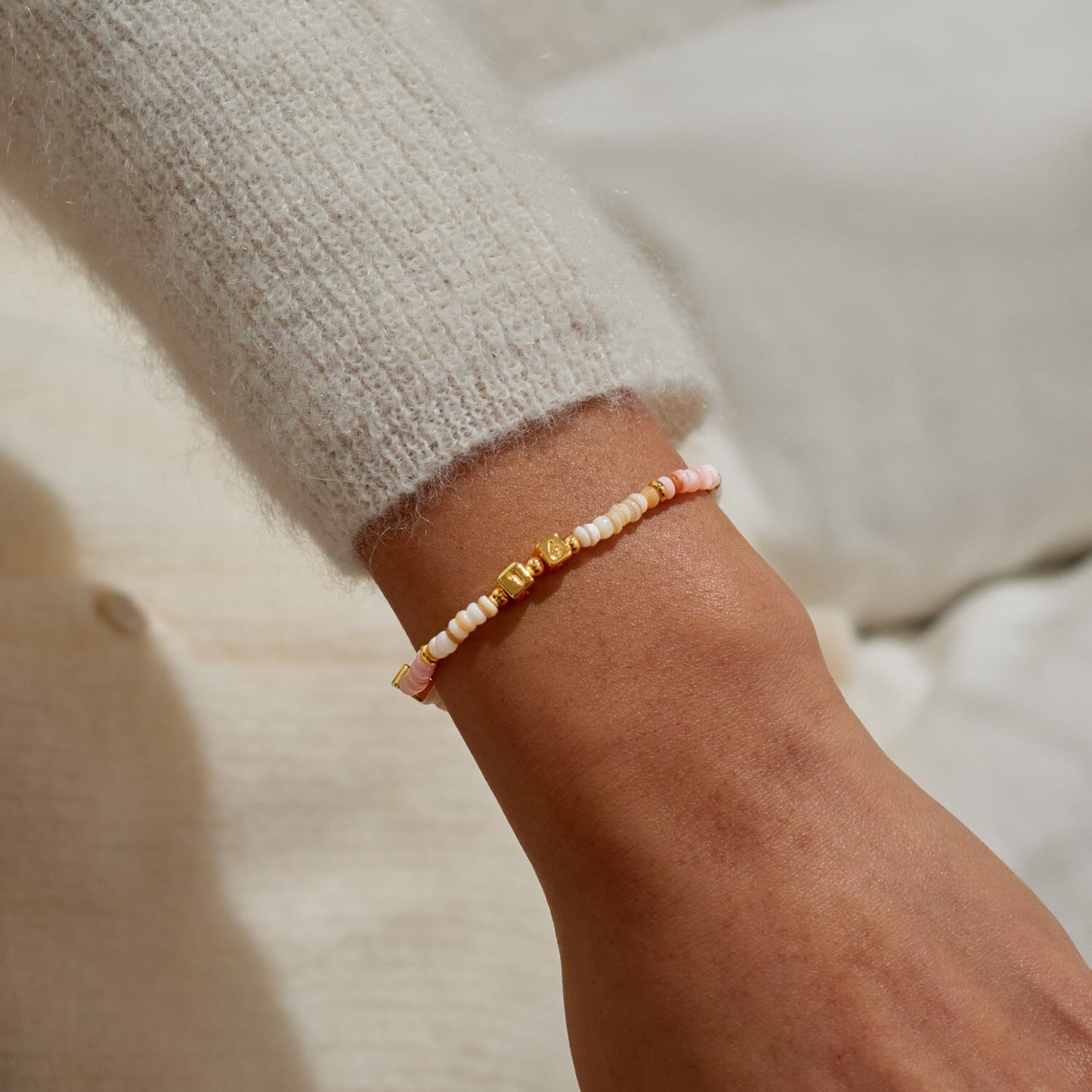 Close-up of a wrist wearing a pink and gold beaded bracelet on a neutral background