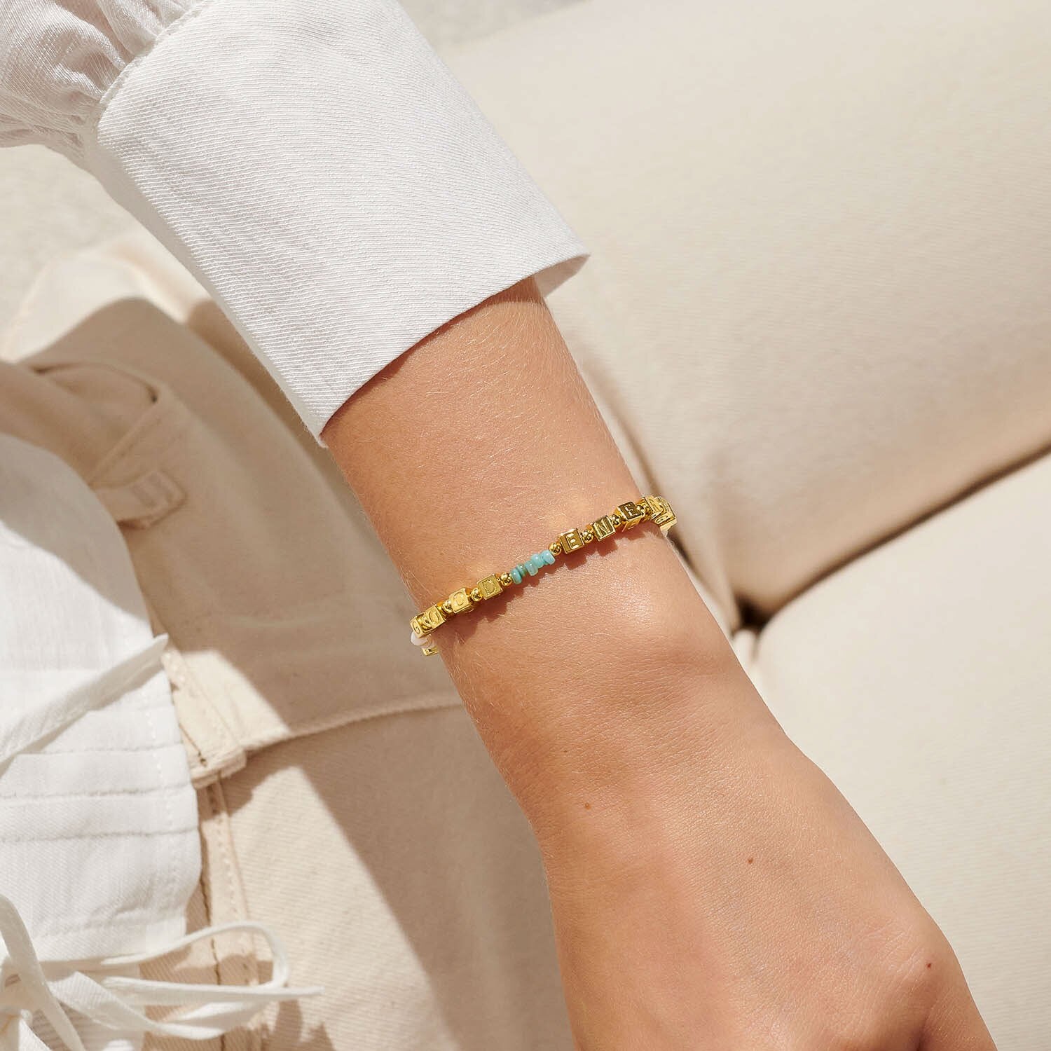 Gold bracelet with colorful beads on a person's wrist against a neutral background