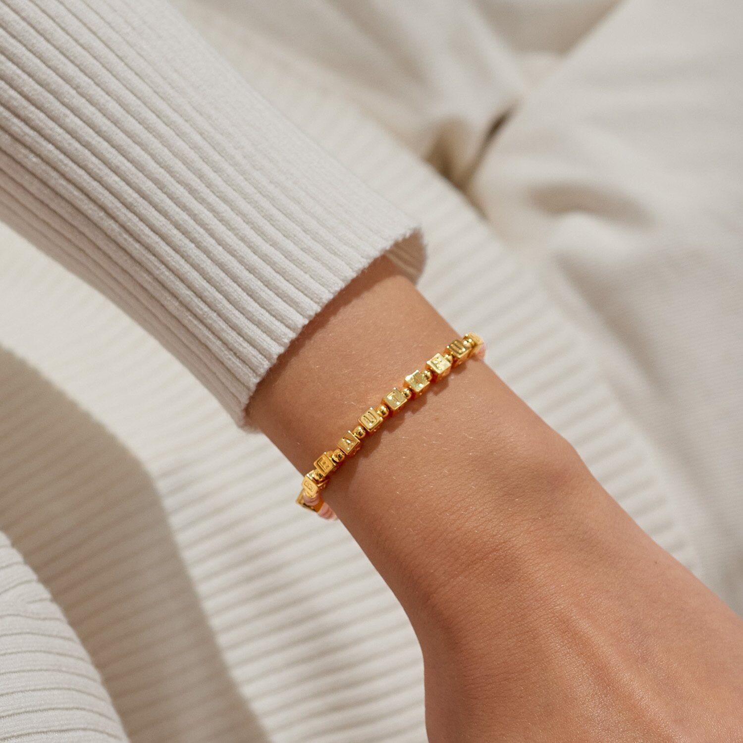 Gold bracelet on a wrist with a neutral background