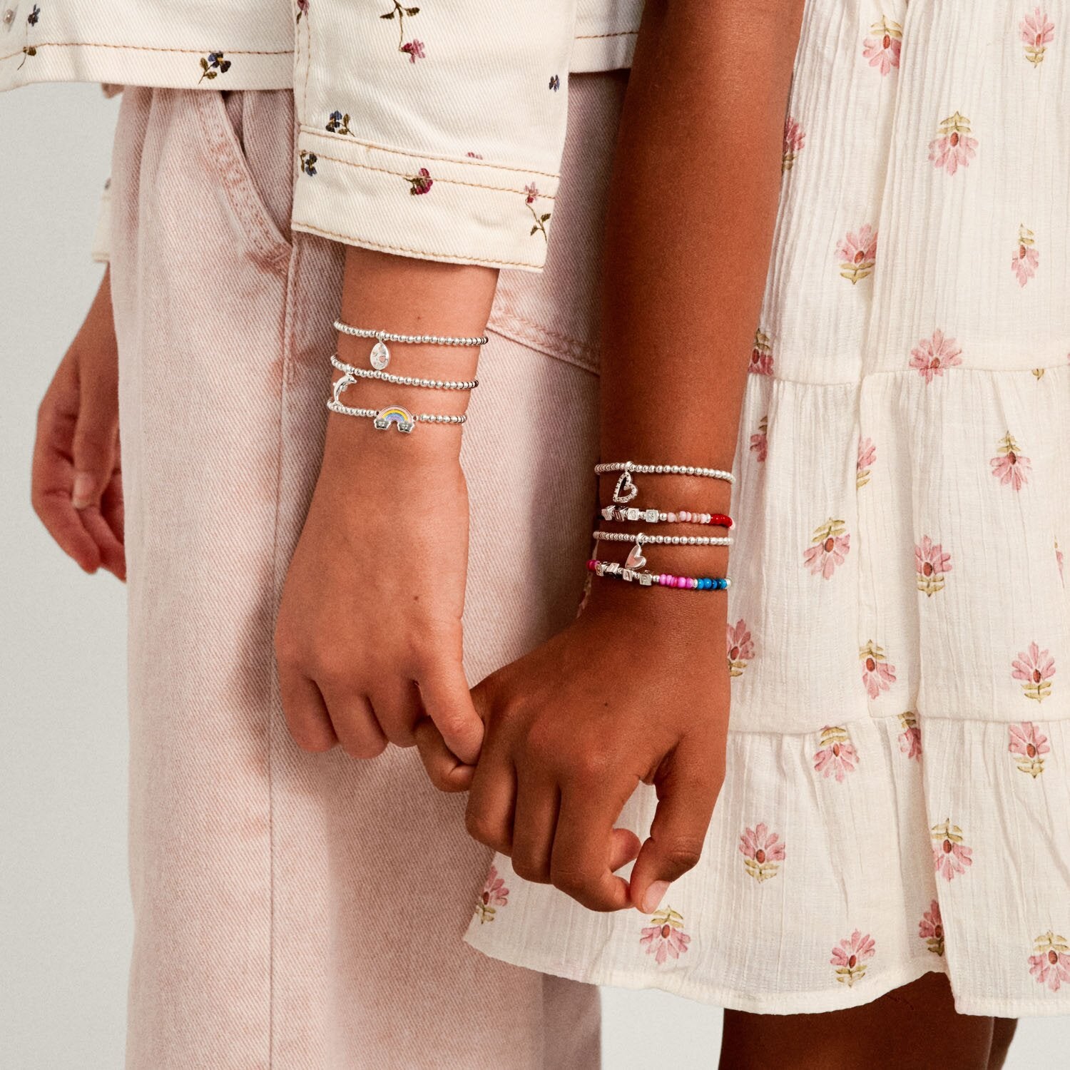 Two people holding hands with bracelets on a light background