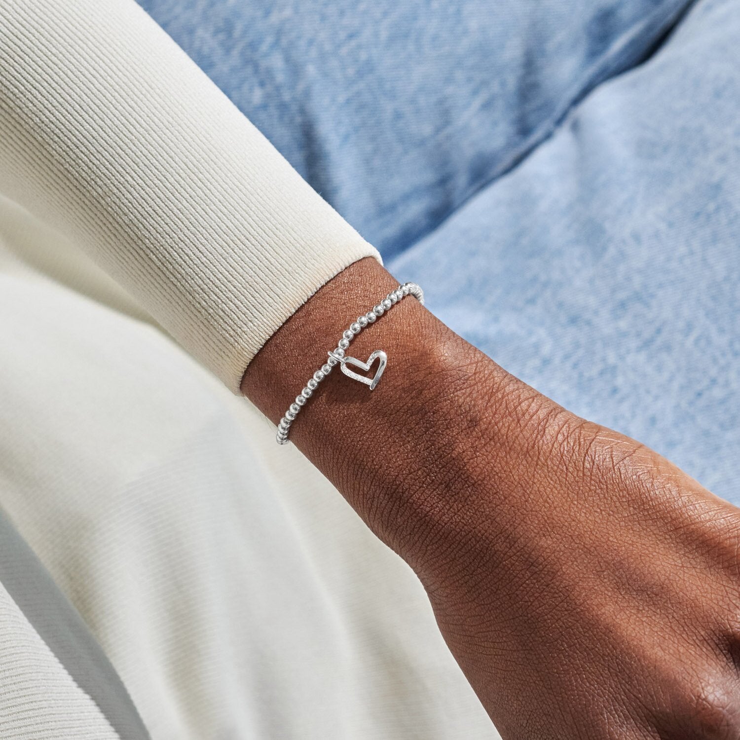 Silver bracelet with a heart charm on a wrist against a neutral background