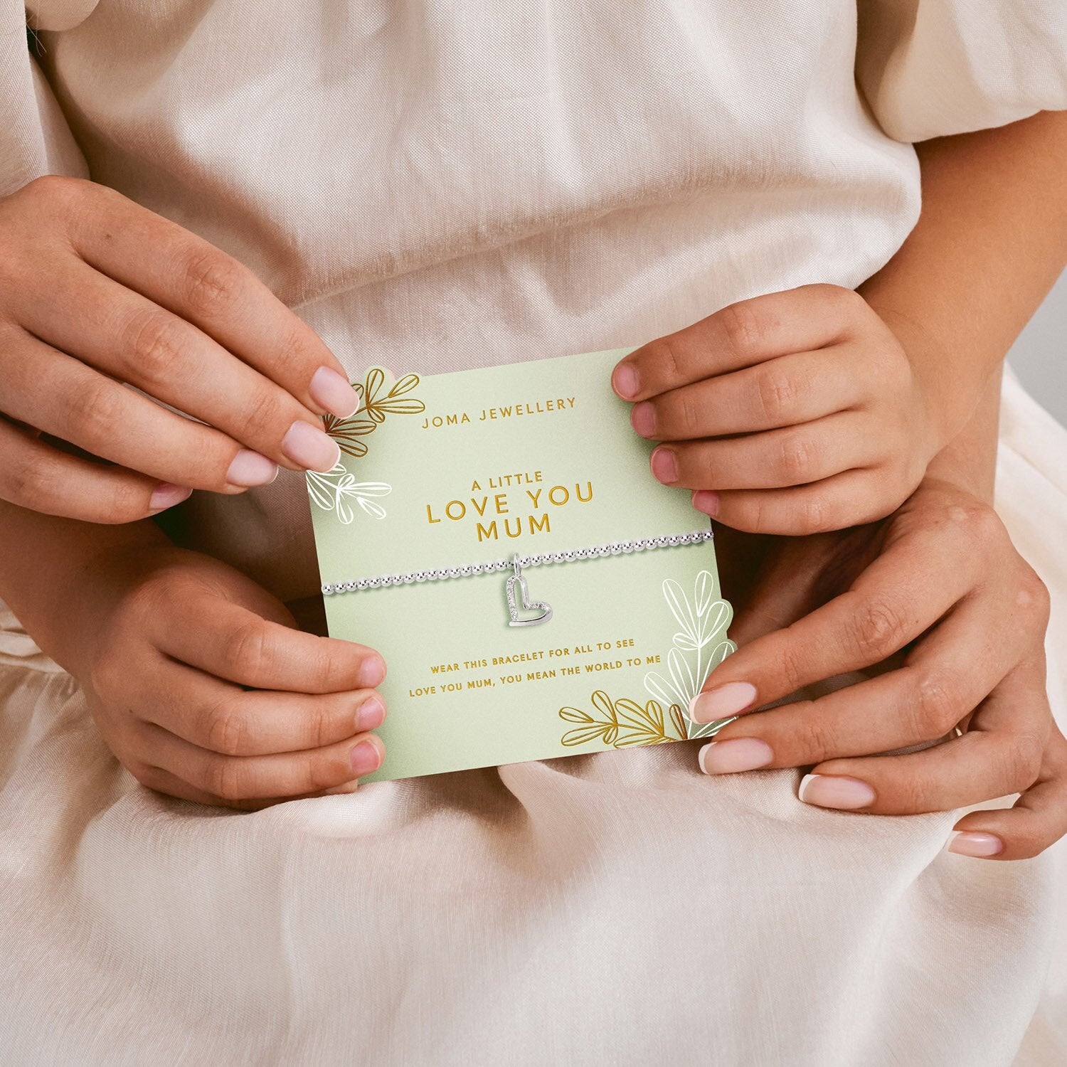 Hands holding a Joma Jewellery card with 'A Little Love You Mum' text.