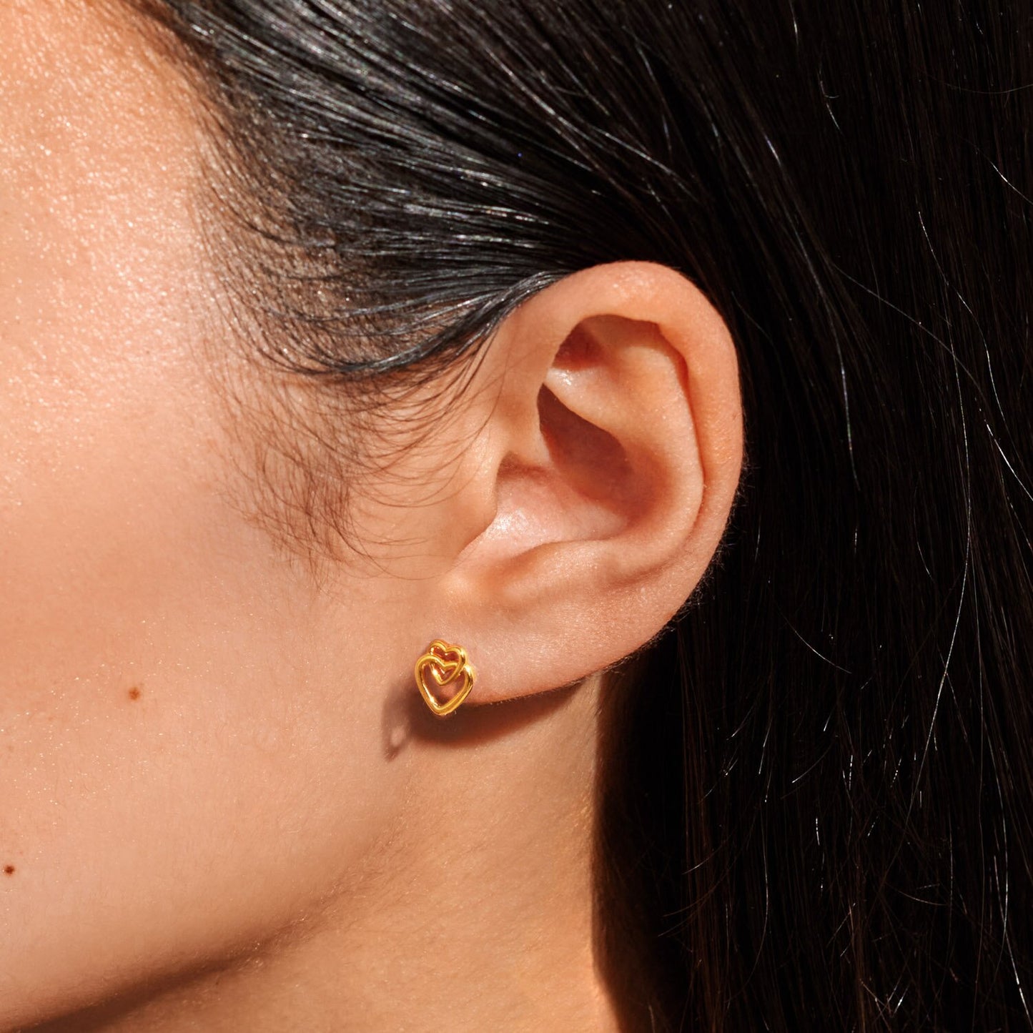Close-up of an ear wearing a gold earring with dark hair in the background