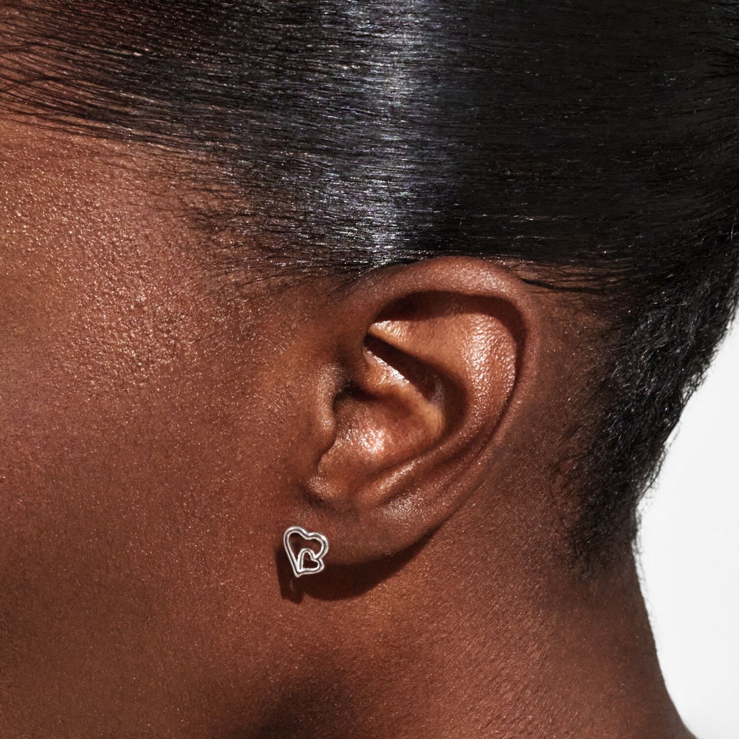Close-up of an ear wearing a heart-shaped earring with a neutral background