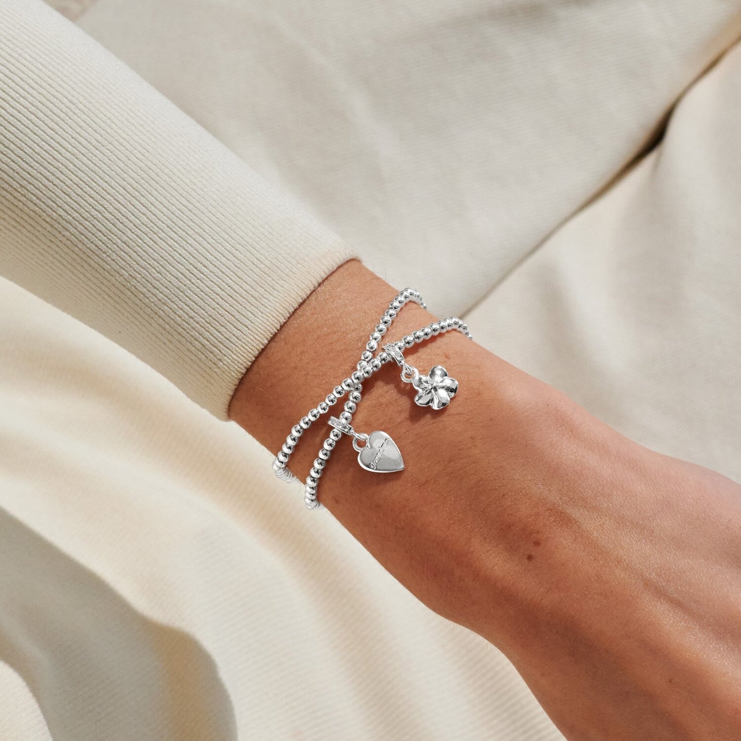 Silver bracelet with charms on a wrist against a beige background