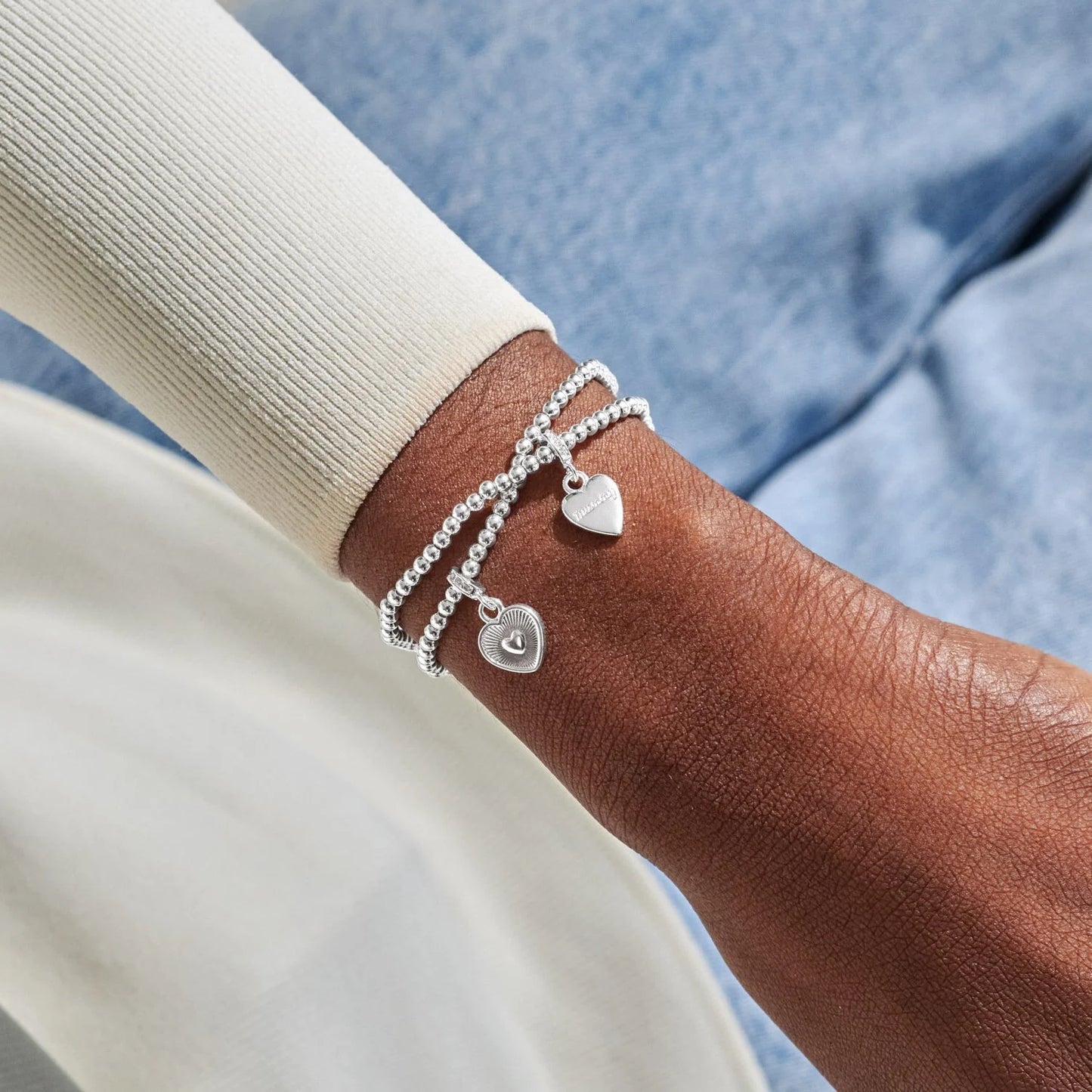 Silver bracelet with heart charms on a wrist against a blue denim background