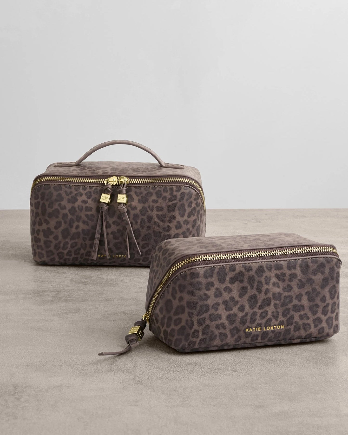 Two leopard print toiletry bags with gold zippers on a neutral background