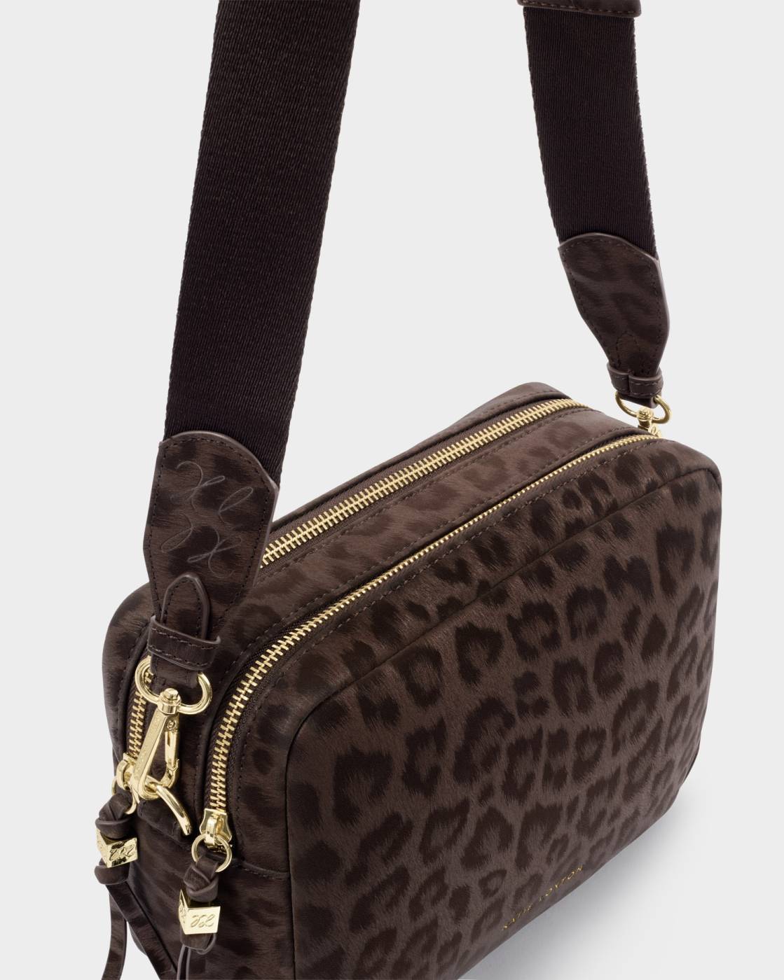 A brown and black leopard print crossbody bag with gold-tone hardware and a wide black fabric strap, shown against a light gray background.