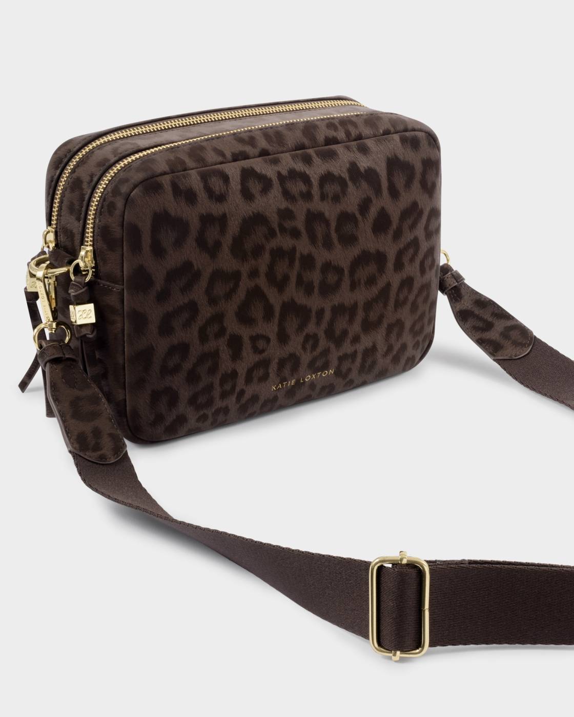 A Katie Loxton crossbody camera bag in dark brown leopard print nylon with gold-tone hardware and a matching adjustable shoulder strap, shown on a light grey background.
