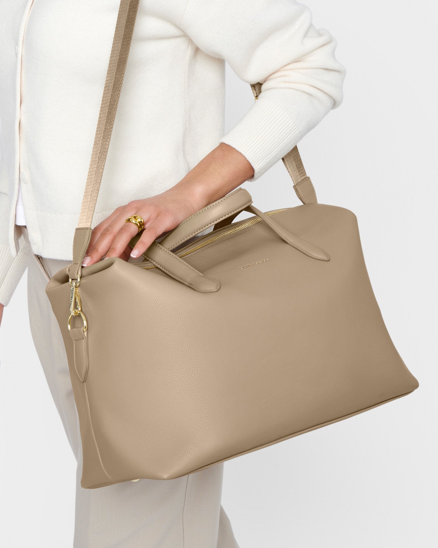 Beige handbag held by a person wearing a white outfit on a light gray background