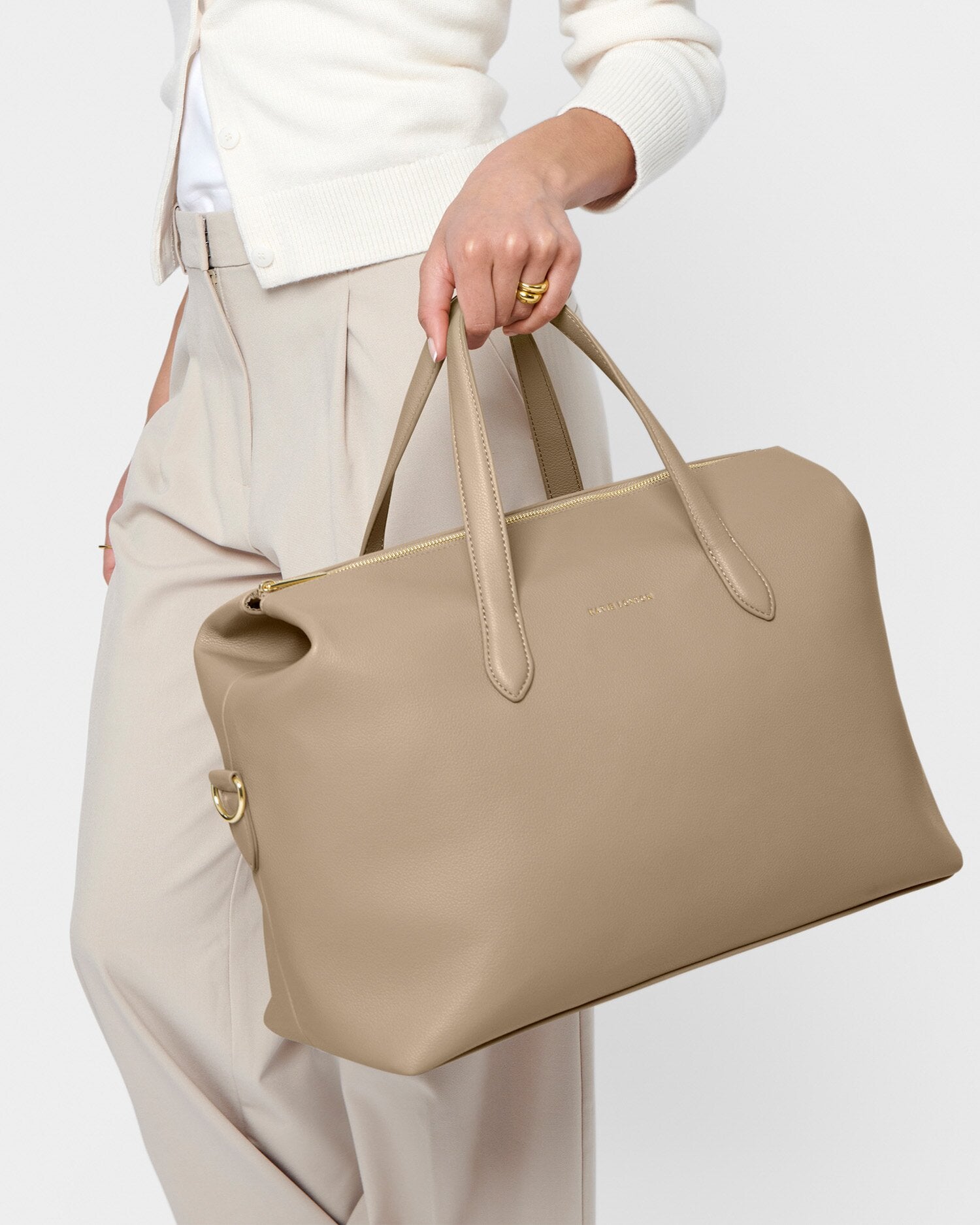 Beige handbag held by a person against a white background