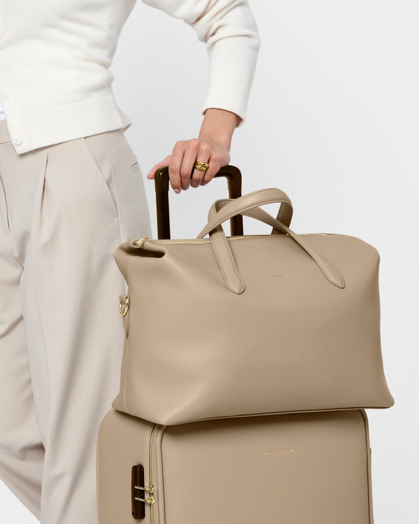Person holding a beige handbag over a suitcase on a white background