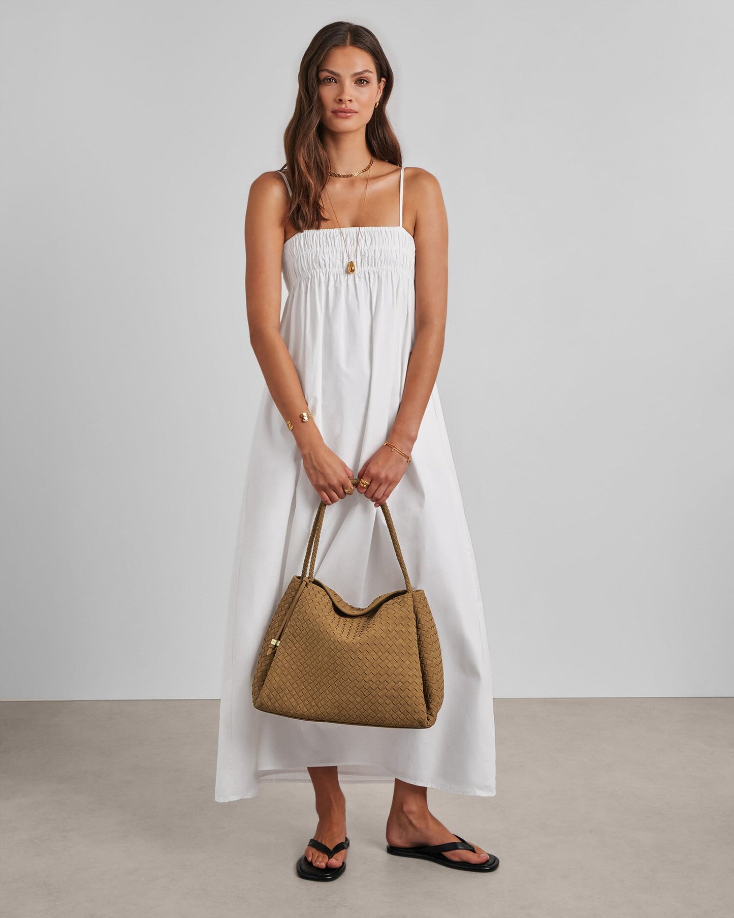 Woman in a white dress holding a brown handbag against a plain background