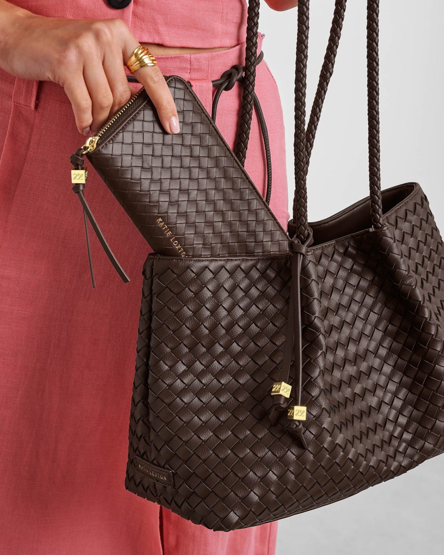 Brown woven handbag held by a person wearing pink pants